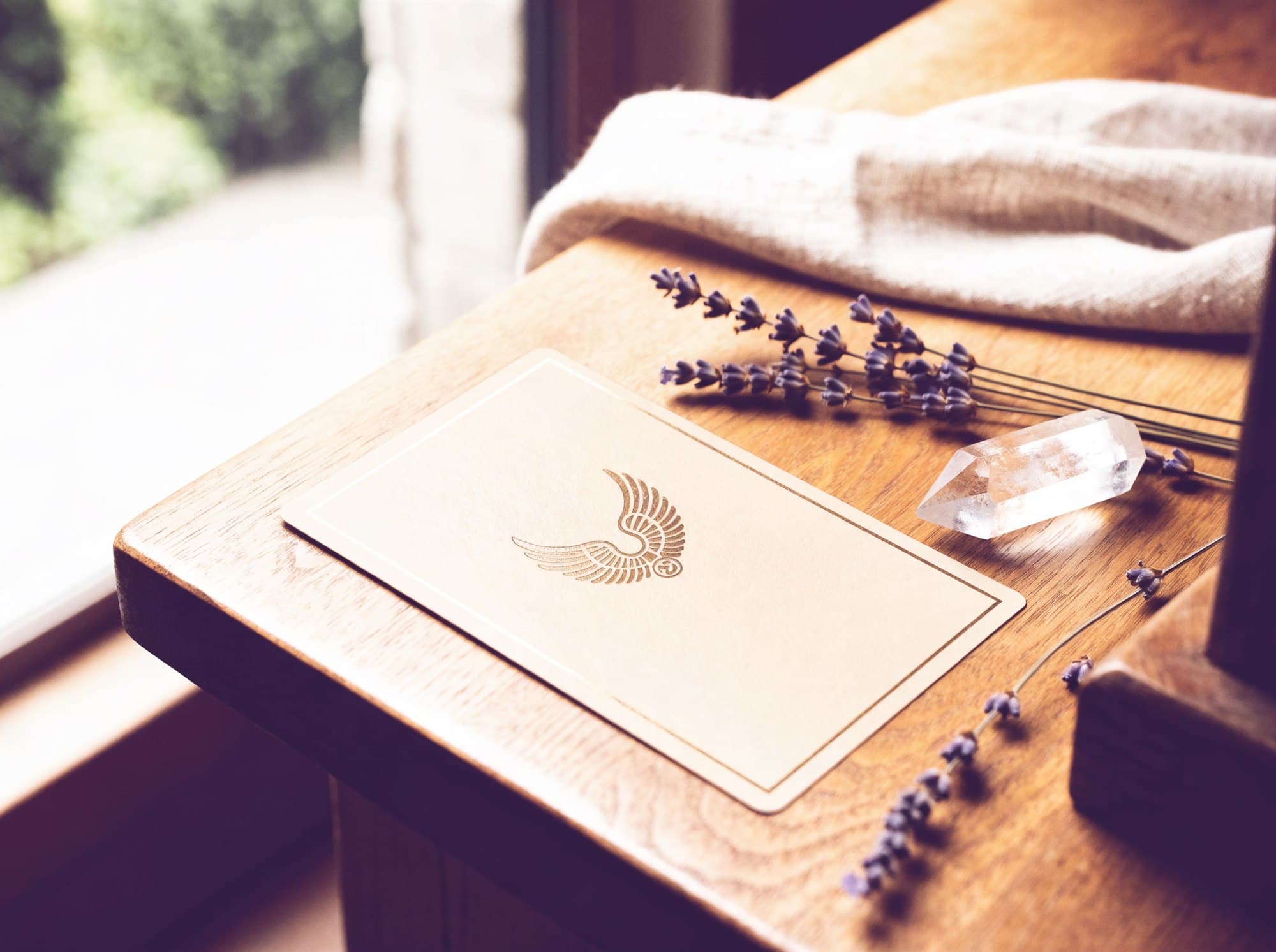 A single angel oracle card on a wooden table beside a clear quartz point and dried lavender